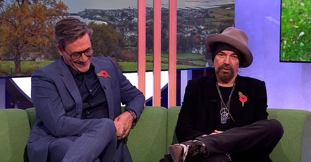 two men in suits and hats are sitting on a green couch