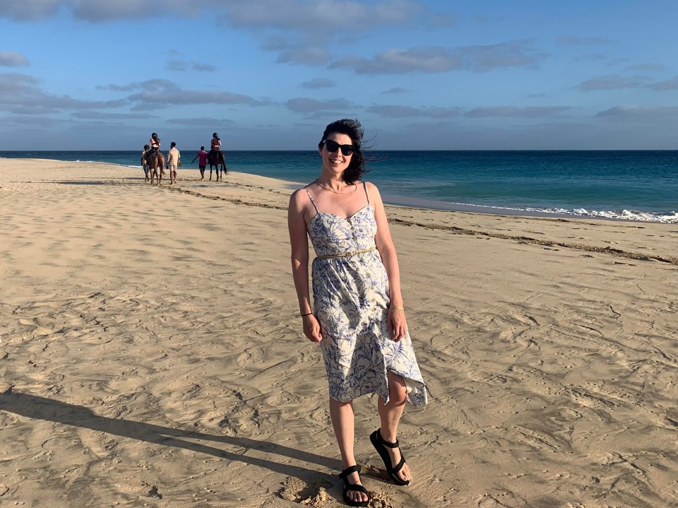 a woman stands on a sandy beach with horses in the background