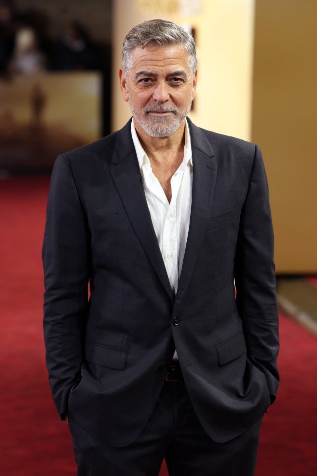 a man in a suit stands on a red carpet with his hands in his pockets