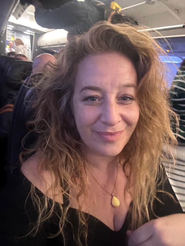 a woman wearing a black top and a gold necklace smiles for the camera