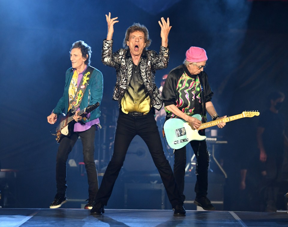three men are playing guitars on a stage and one of them is wearing a pink hat