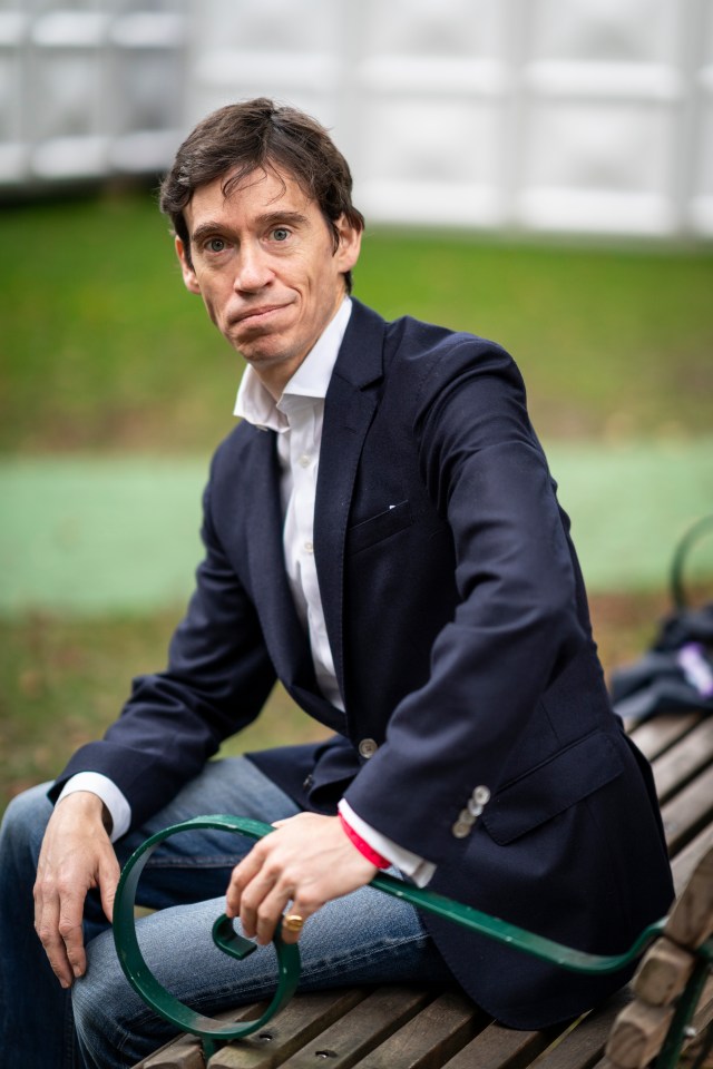 a man in a blue jacket sits on a wooden bench