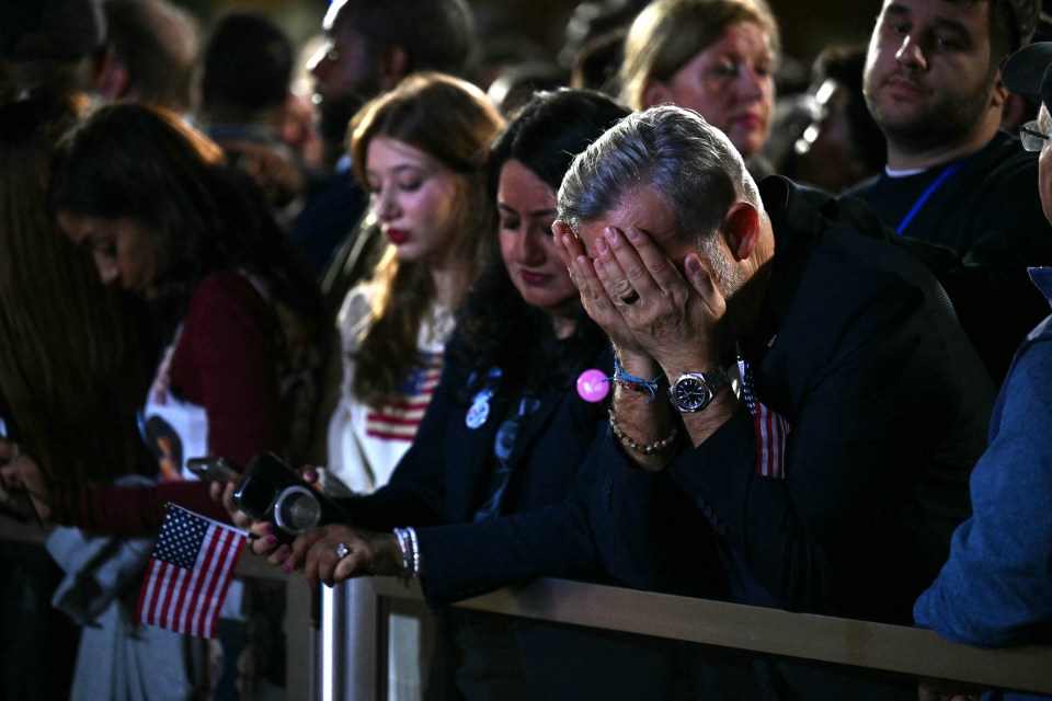 a man covering his face with his hands in a crowd of people