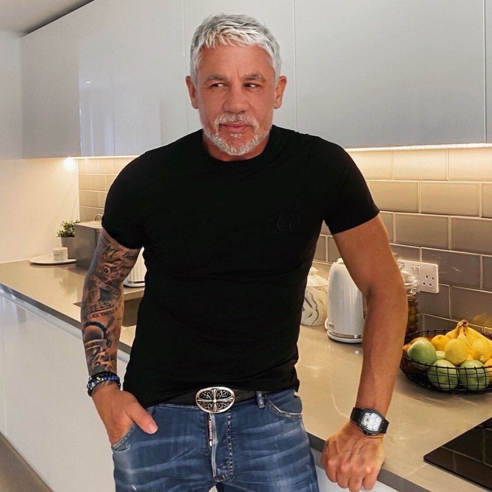 a man in a black t-shirt and blue jeans is standing in a kitchen