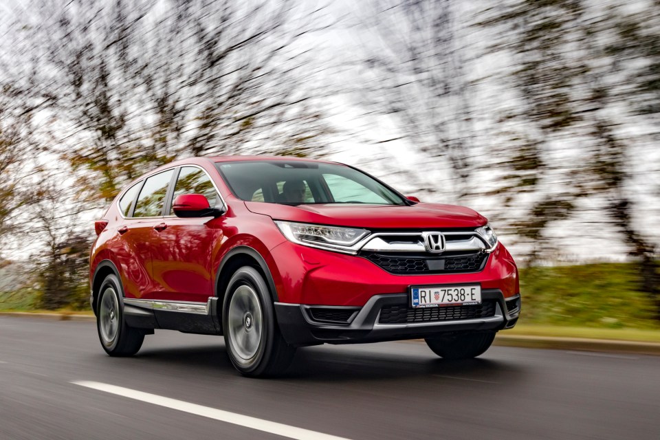 a red honda cr v is driving down a road