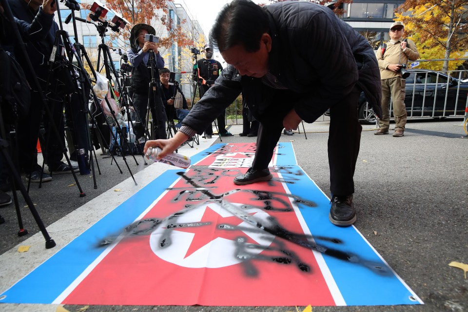 A South Korean protester spray paints on a North Korean flag during an anti-North Korea rally