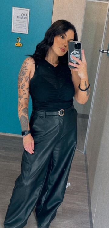 Woman in black top and leather pants taking a selfie.