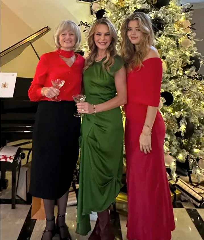 Three women in holiday dresses pose by a Christmas tree.