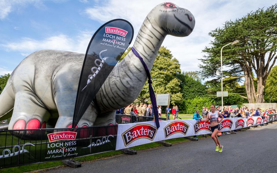 A female runner finishes the Baxters Loch Ness Marathon, running past a large inflatable Loch Ness Monster.