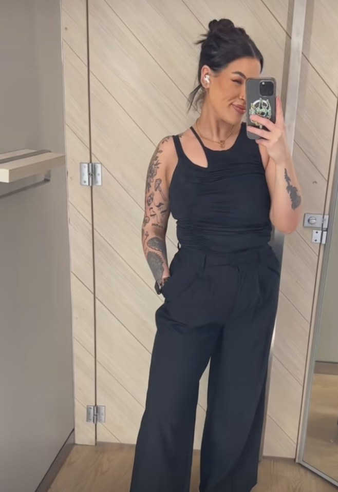 Woman with tattoos taking a selfie in a black top and pants.