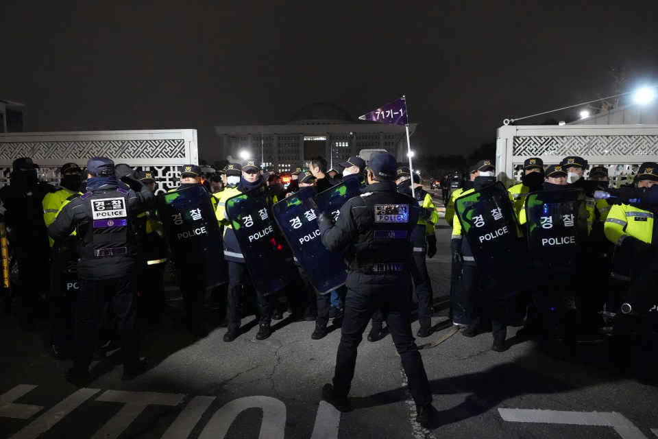 Police officers stand guard as the furious crowds try to get through the main gates