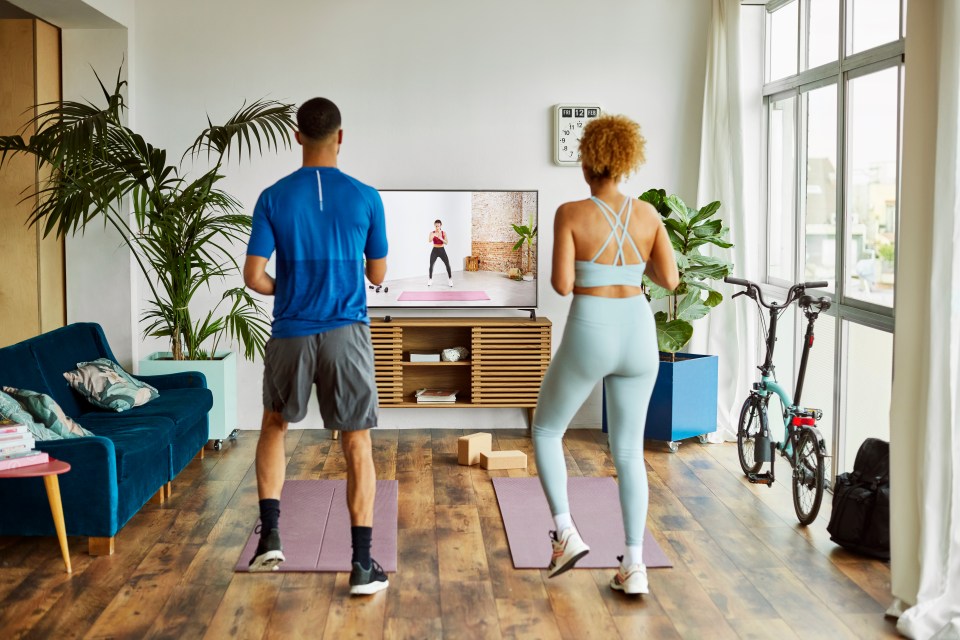 Couple following online workout class on TV in their living room.
