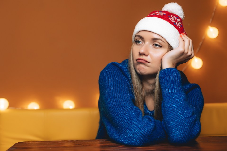A sad-looking teenage girl wearing a blue sweater and Santa hat.