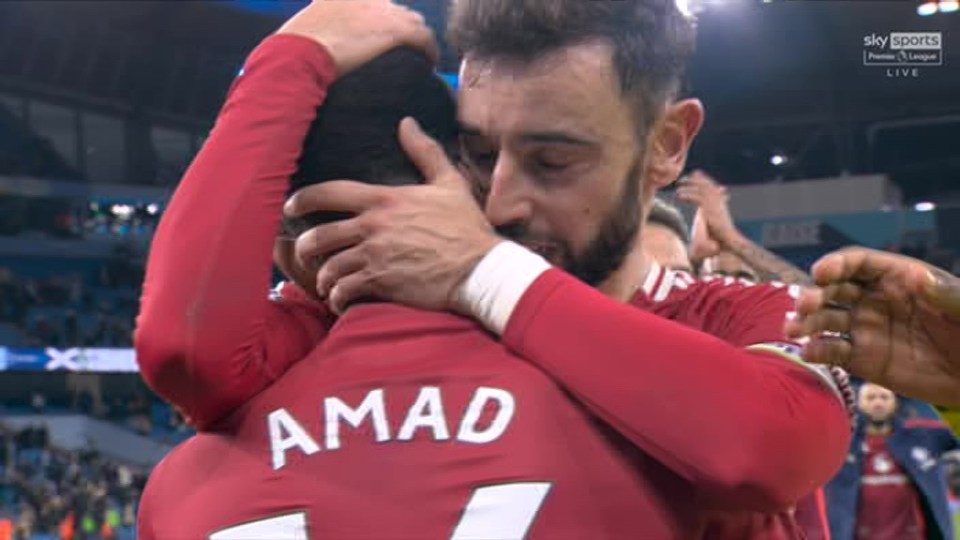 Two soccer players in red jerseys embrace after a goal.  Amad's name is visible on one jersey.