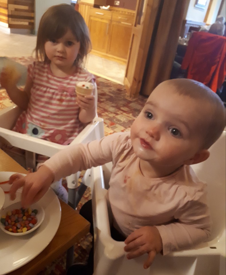 Two young girls sitting in high chairs, eating.