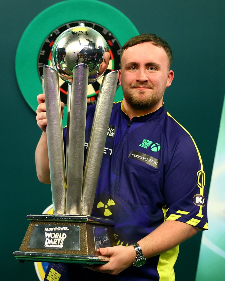 Luke Littler holding the PaddyPower World Darts Championship trophy.