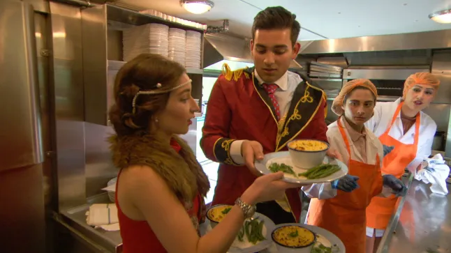 A waiter in a red jacket serves a woman in a red dress a dish of food.