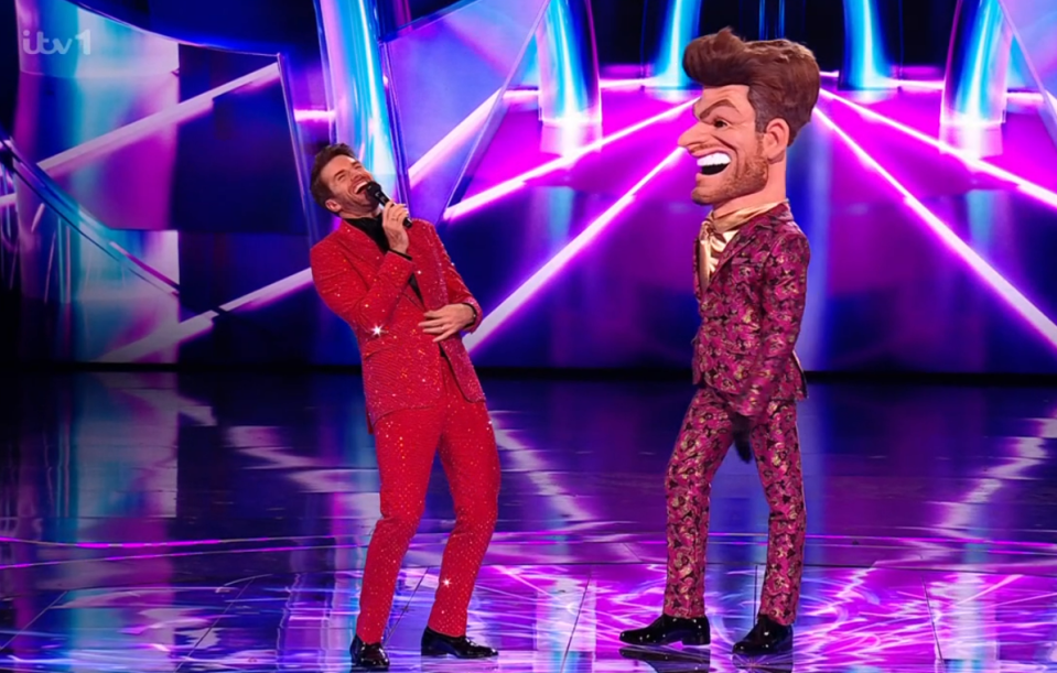 A man in a red sequined suit sings alongside a large-headed caricature in a patterned suit.