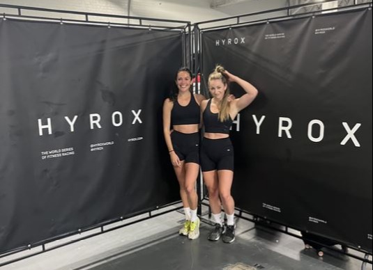 Two women posing at a Hyrox fitness competition.
