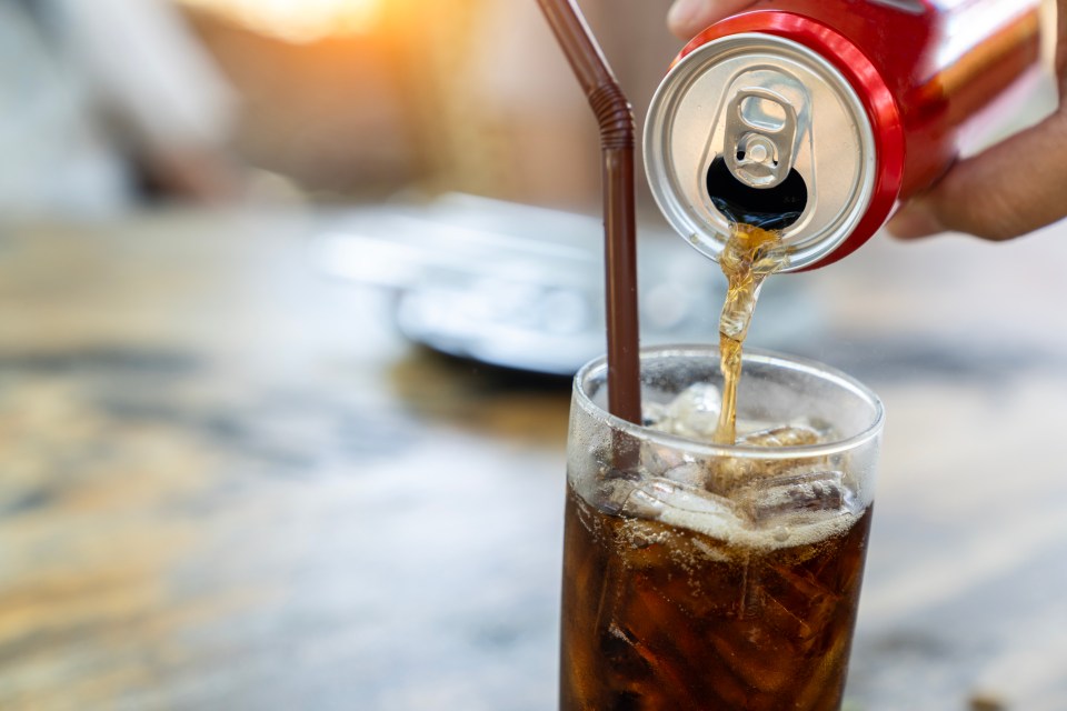 Pouring soda from a can into a glass with ice.