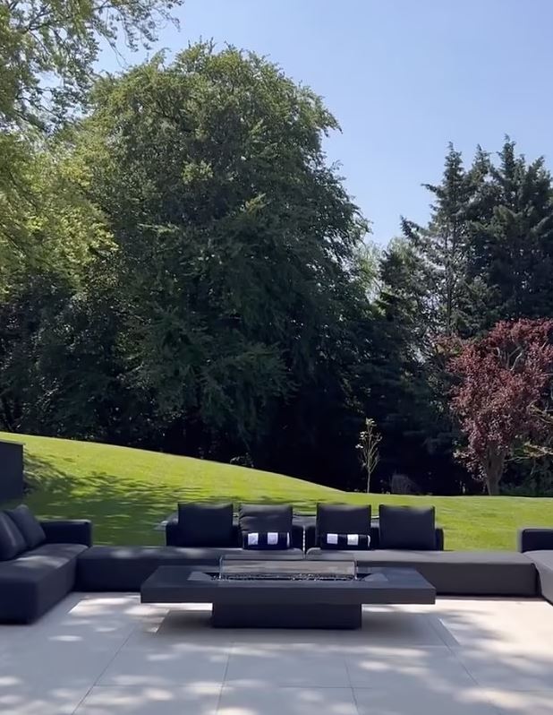 Outdoor patio furniture with fire pit and green lawn in the background.