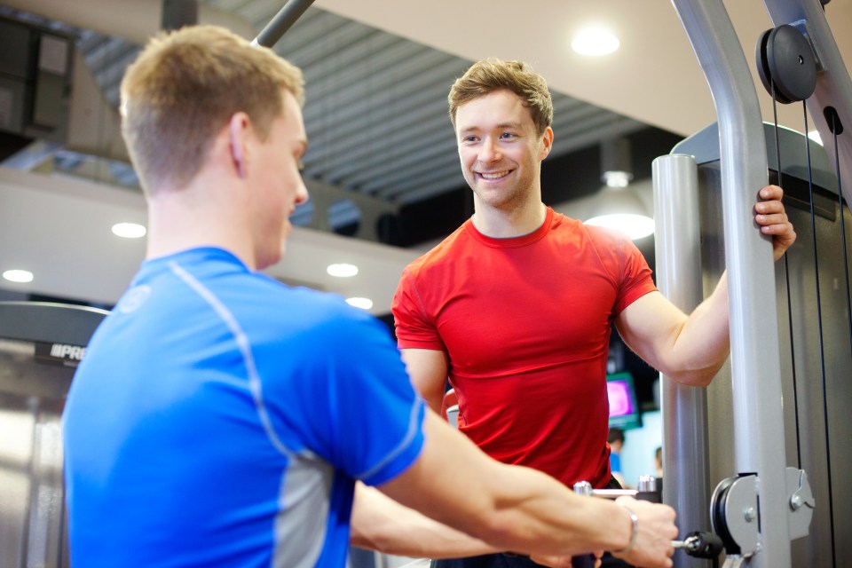 Personal trainer assisting a man using a weight machine at the gym.