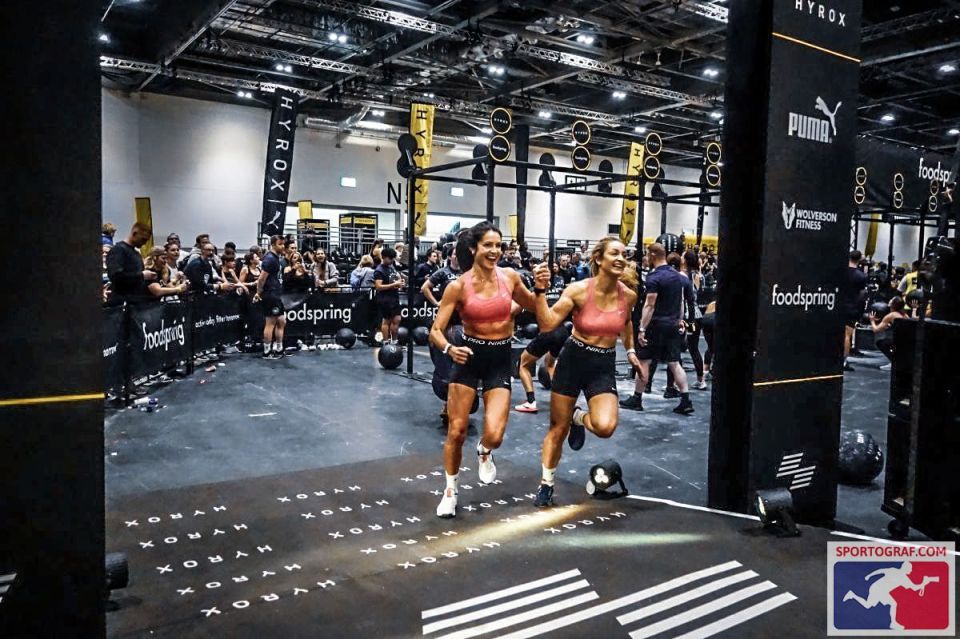 Two women smiling and running during a Hyrox competition.