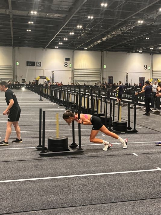 Woman pushing a weighted sled during a Hyrox competition.