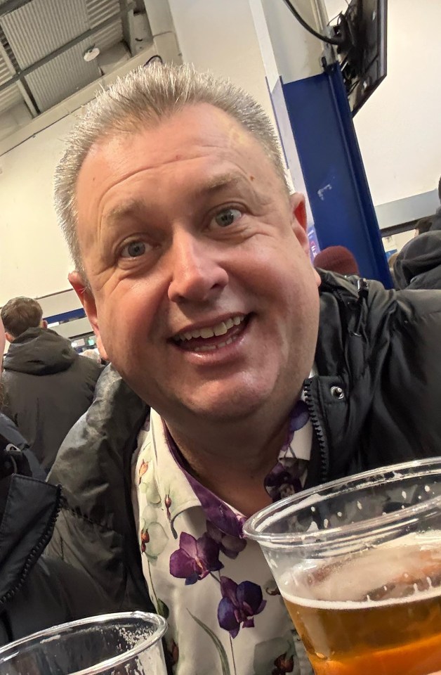 Two men at a sporting event holding beers and smiling for a selfie.