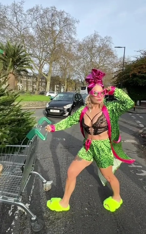 A woman in a bright green leopard-print outfit pushes a shopping cart with a Christmas tree while wearing bright yellow slippers.