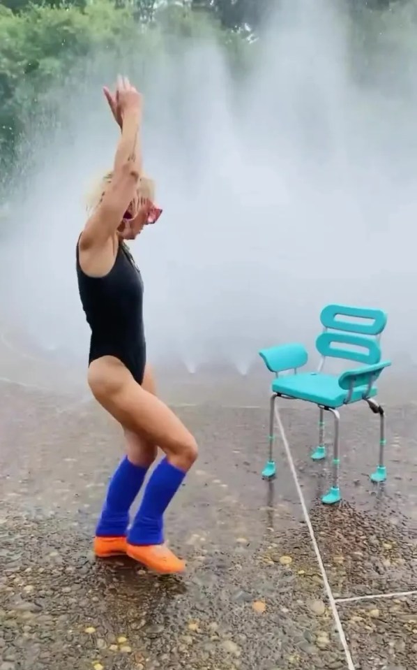 Woman in leotard and leg warmers dances by a fountain, next to a shower chair.