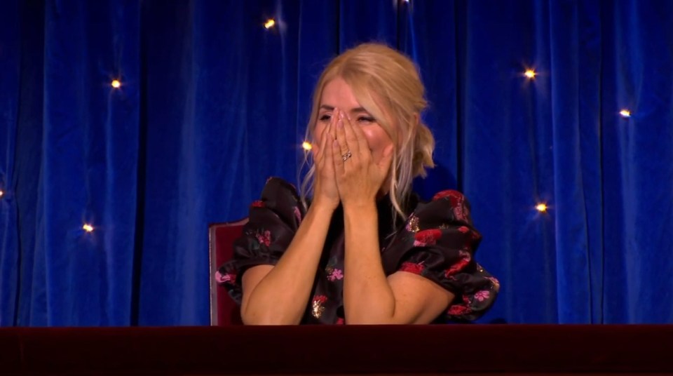 Woman covering her face with her hands while sitting in front of a blue curtain.