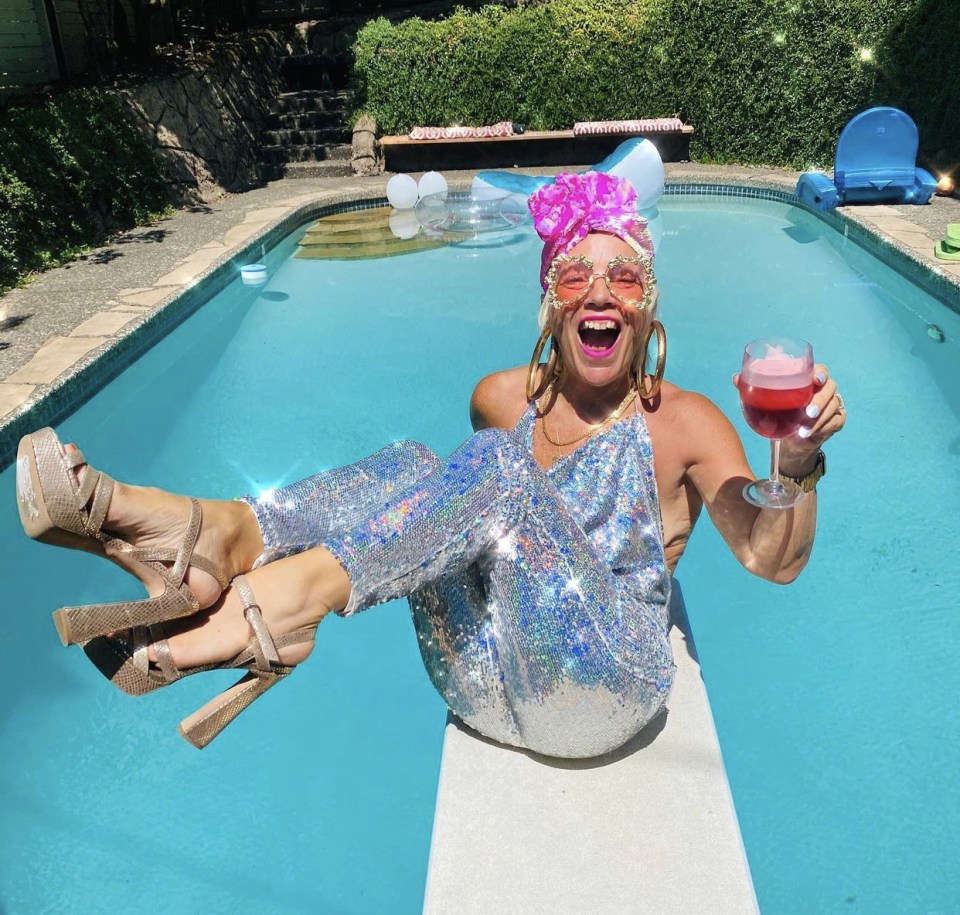 Woman in sequined jumpsuit in a swimming pool holding a drink.