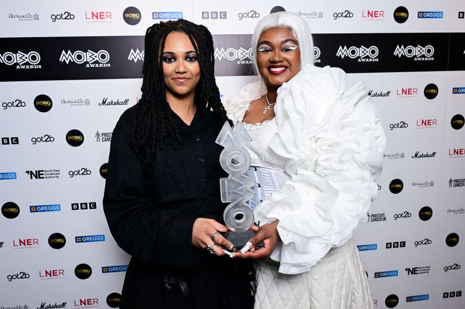 Nyrobi Beckett-Messam and Chaya Beckett-Messam of ALT BLK ERA holding a MOBO Awards trophy.