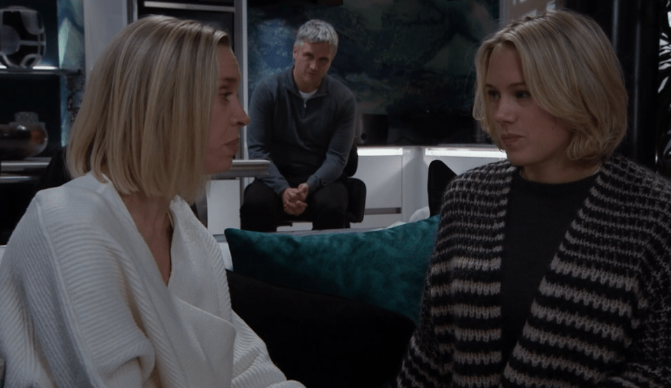 Two women talk while a man sits in the background.