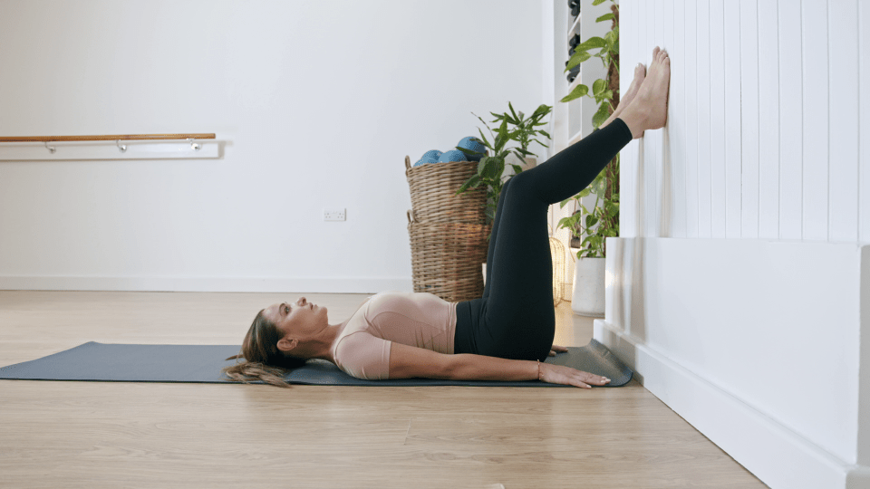 Woman doing Pilates exercise with legs against wall.