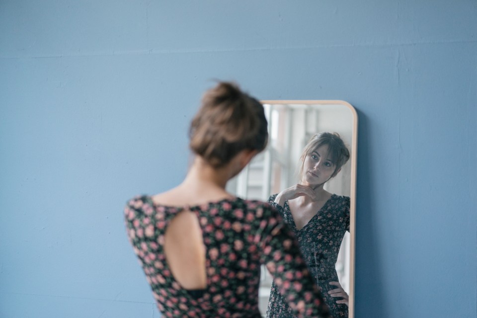 Woman in floral dress looking in mirror.