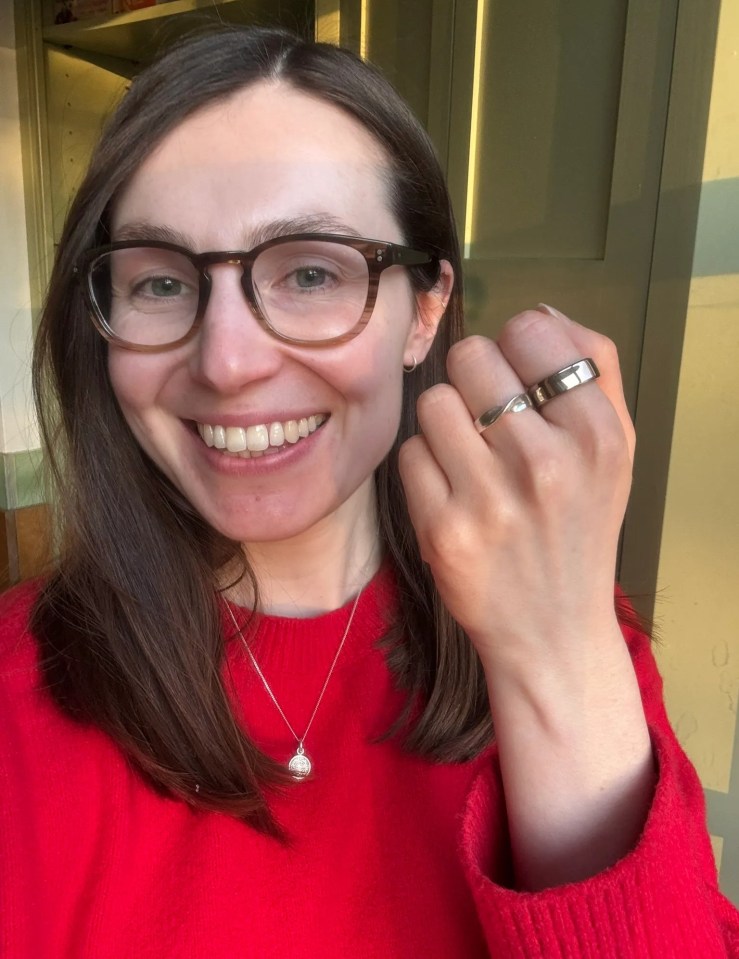 Woman wearing glasses and a red sweater shows off two rings.