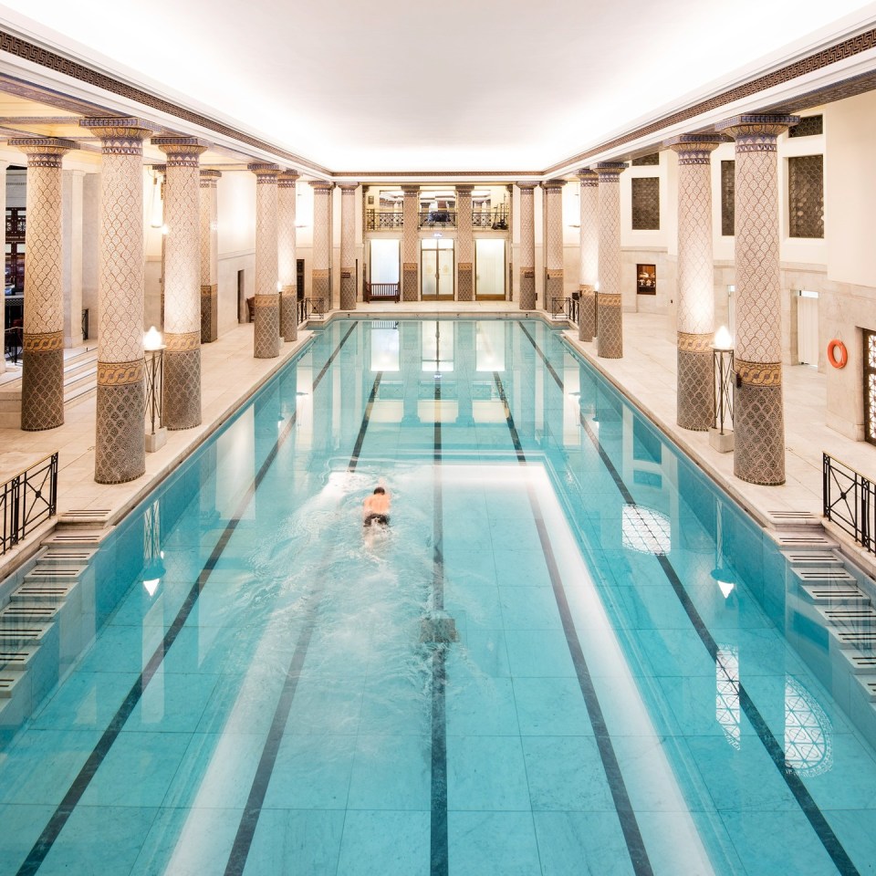 A man swimming in a Grecian-inspired indoor pool.