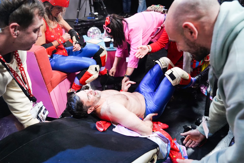 A man lies on the floor surrounded by people during a Red Nose Day fundraising event.