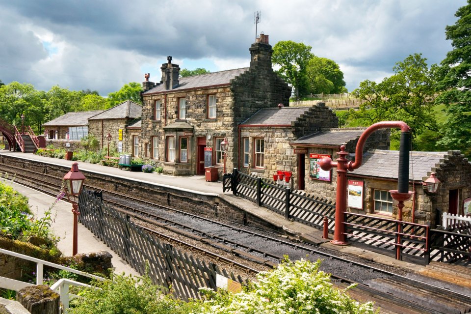 Stone railway station building with tracks and fences.