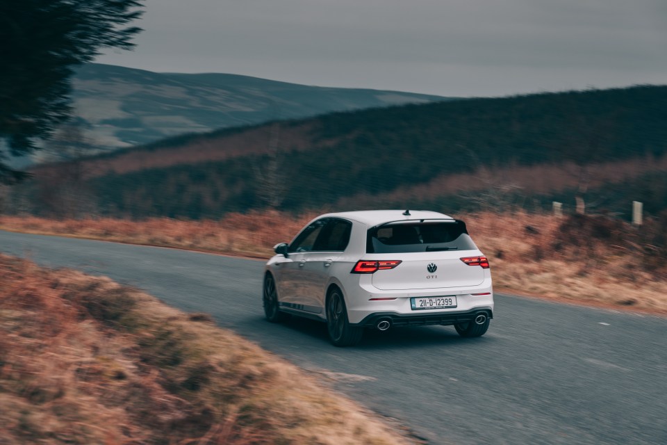 White Volkswagen Golf GTI driving on a mountain road.