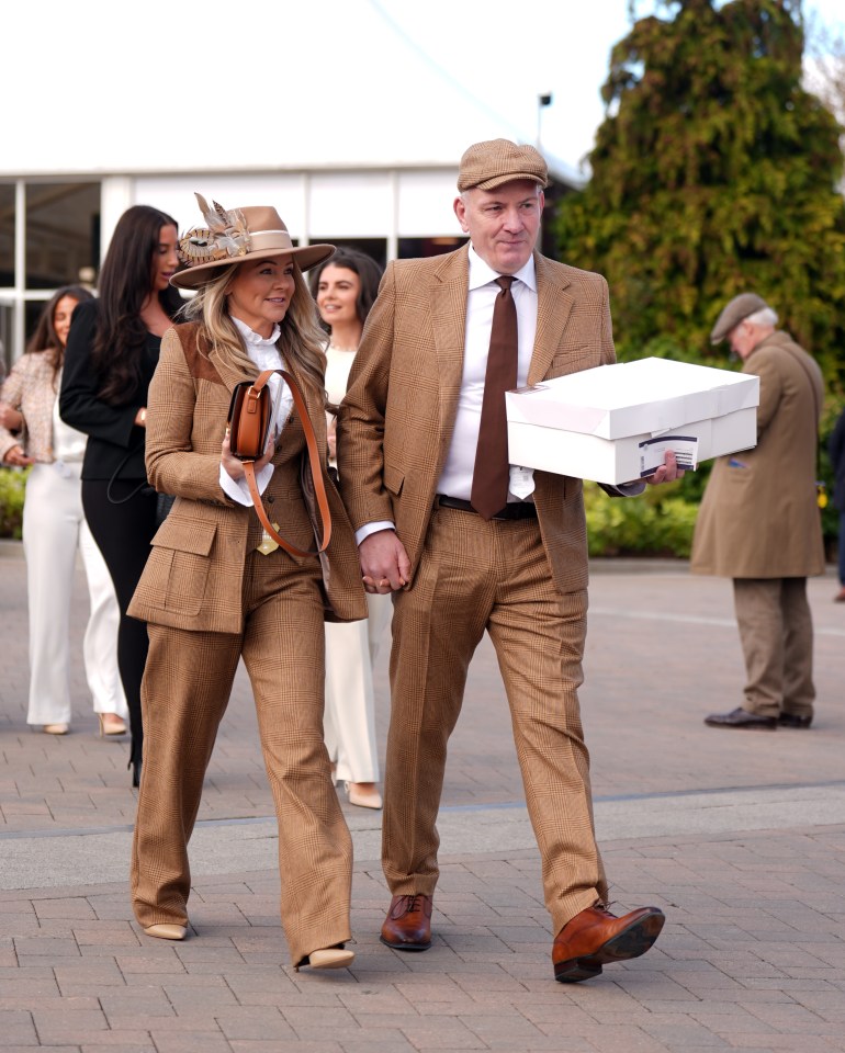 Couple in matching brown suits walking at a horse race.