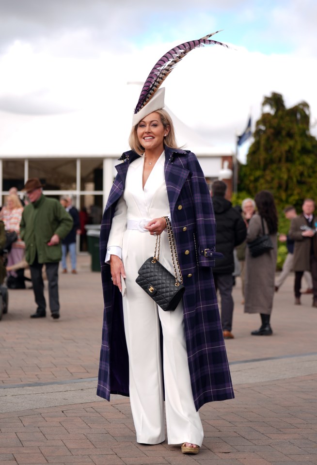 Woman in white jumpsuit and purple plaid coat at a horse race.