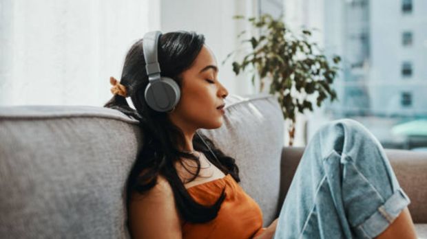 Woman listening to headphones on a couch.