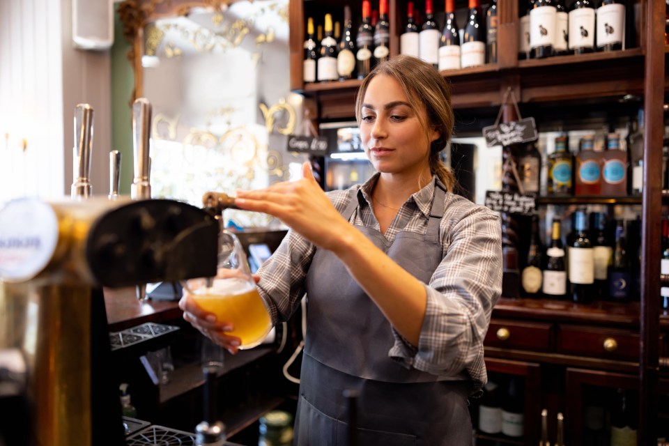 Beautiful female bartender serving beer from the tap at the pub - food service occupation concepts