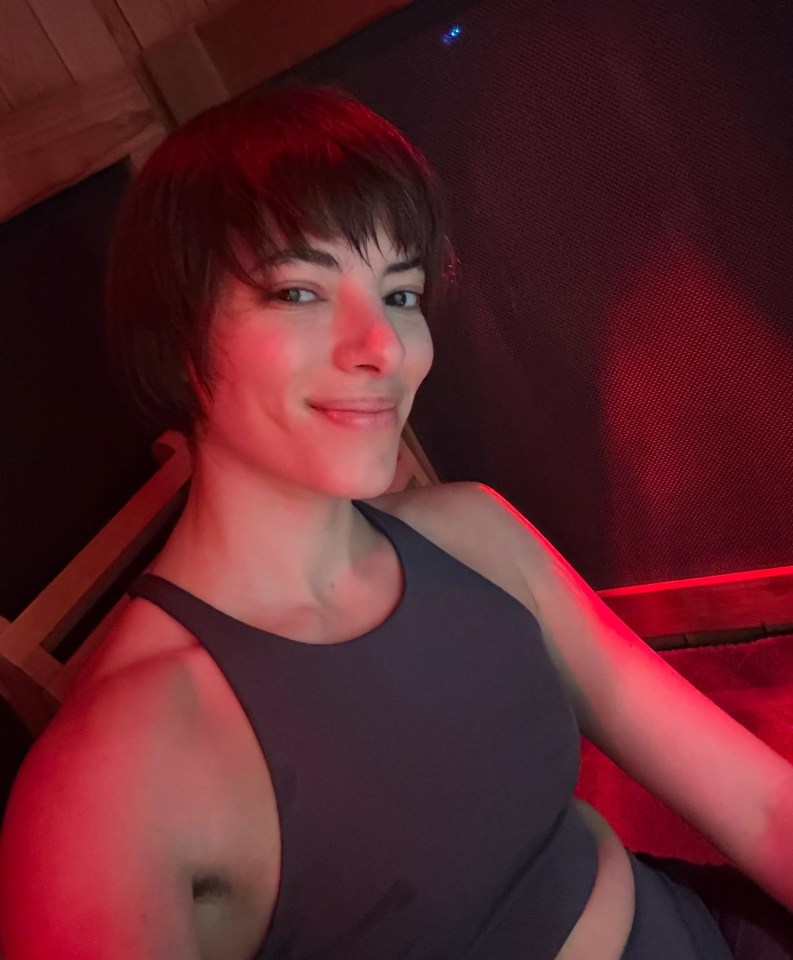 Person in a dark gray sports bra smiling in a red-lit room.