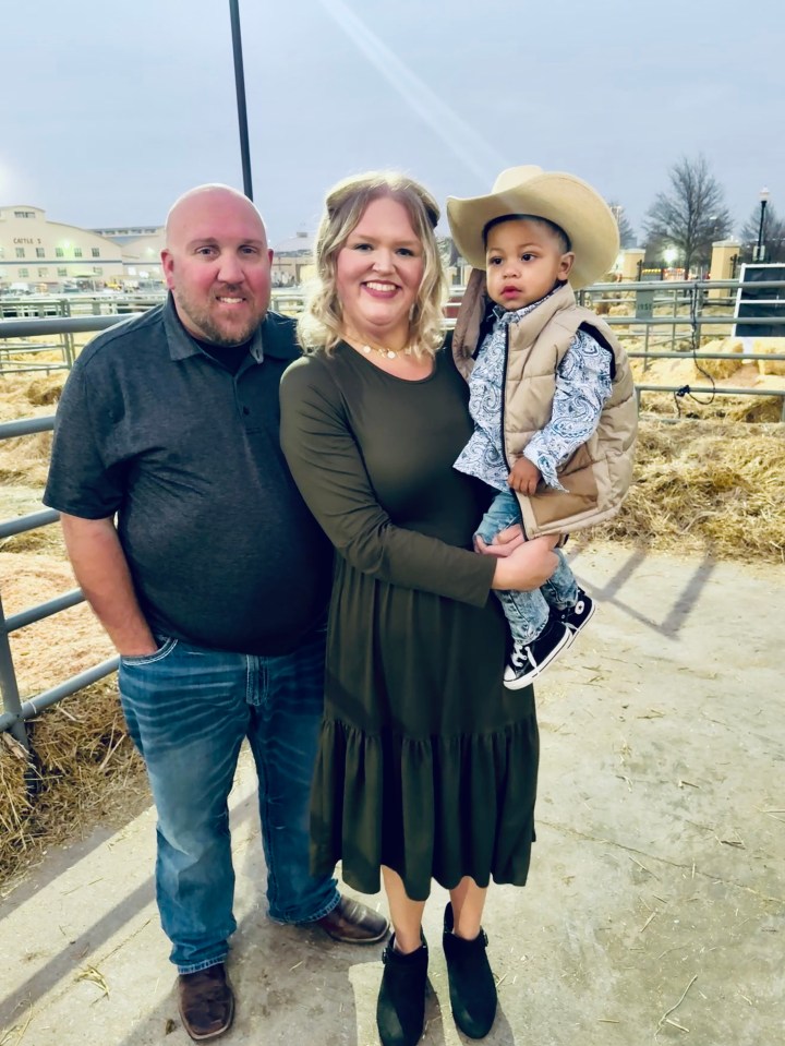A woman, man, and toddler son stand together outdoors.
