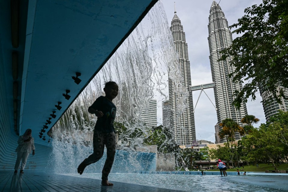 Child playing in a public pool with the Petronas Twin Towers in the background.