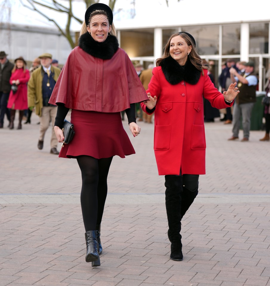 Two women in red outfits walking at a horse race.